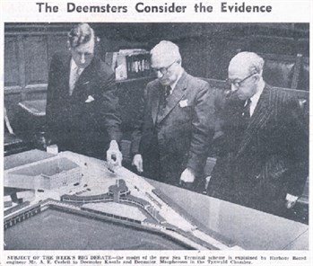  Mr A.E Corlett, standing at a table with Deemster Kneale and Deemster Macpherson looking at a model of the sea terminal on the Isle of Man.