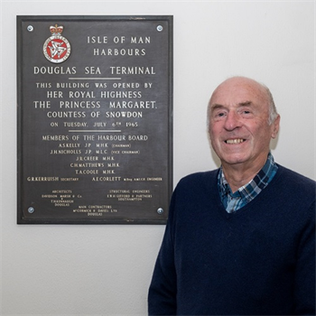 Robin Corlett standing next to the plaque at the sea terminal on the Isle of Man commemorating the opening of the sea terminal in 1965 by Princess Margaret.