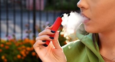 Woman blowing smoke while holding vape
