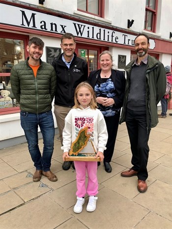 Kayleigh Cannon winner of the Young Nature Writer stadning outside the manx wiildlife trust holding her trouphy with representatives of the competition standing behind her