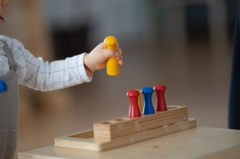 Picture showing a young child playing with a wooden toy, they are holding a yellow toy in their hand