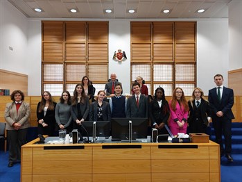 12 students from the Islands secondary schools standing in court room 3 with three of the Island’s Magistrates standing up behind them.