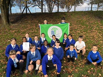 A group of students from St Mary’s primary school sitting on grass, with two students standing behind the group holding a green eco schools flag