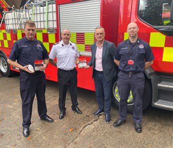 Members of the Isle of Man Fire and Rescue Service (IOMFRS) with a representative from Tower Insurance standing in front of a fire engine holding smoke alarms, which Tower has donated as part of the fire safety partnership.
