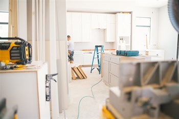 Image showing builders constructing a kitchen in a new house build. The picture shows a tool box on top of a white kitchen island, with white lower and upper cupboards.