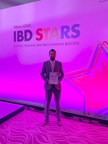 Greg Manning standing infront of a sign that says Titotts logic, IBD Stars. Support, Training and Recognising success. He is hold The Rising Star Award 2023